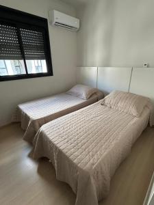 two beds in a bedroom with a window at Ap Novo Parque Anchieta - Top in Pelotas