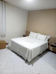 a bedroom with a white bed with white sheets and pillows at Pousada Colonial in Macaé +2 photos