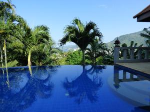 a swimming pool with palm trees and a mountain in the background at Baiyok Villa seaview and edge pool in Patong Beach