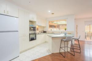 una cucina con armadi bianchi e 2 sgabelli di Well-Appointed Family Home in Popular Location a Tarneit