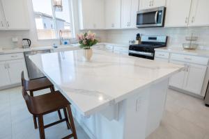 a white kitchen with a large white island with a vase of flowers at Modern Charming 4BR Home, Family Friendly, Office Space, Fast WiFi, Free Parking in Folsom +42 photos