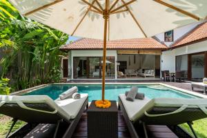 a villa with a swimming pool with chairs and an umbrella at Villa Nolan - Modern 3BR Private Villa with Pool in Padonan, Canggu in Kerobokan