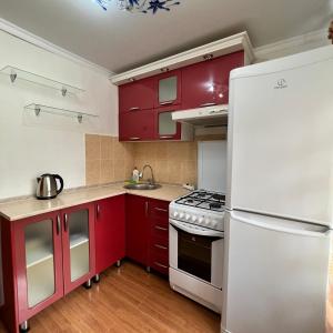 cocina con armarios rojos y nevera blanca en Лободы 34 красиво и уютно, en Karagandá