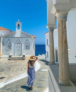 a woman wearing a hat standing in front of a church at Castel Abaso Boutique Apartments by Explore Andros in Andros