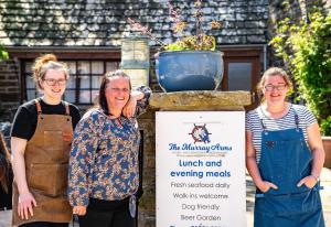 een groep van drie vrouwen in schorten naast een bord bij Murray Arms Hotel and Seafood Restaurant, Orkney in Saint Margarets Hope