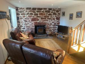 a living room with leather furniture and a stone fireplace at Cranstakie Cottage in Durness
