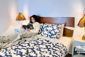 una donna sdraiata a letto che legge un libro di Charming Country House by Ponta Negra Azores a Altares