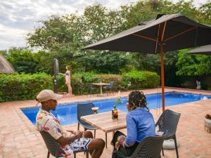 two people sitting under an umbrella by a pool at The Little Outlook in Victoria Falls