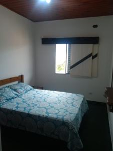 a bedroom with a bed with a blue comforter and a window at Apartamento em Ubatuba Arejado Próximo a Praia in Ubatuba
