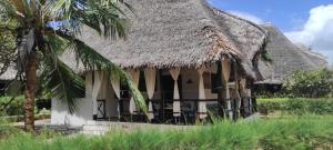 a house with a thatched roof and a palm tree at Karibuni in Malindi