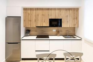 Una cocina con gabinetes blancos y un refrigerador de acero inoxidable. en Apartamentos Julio Burell, 74, en Linares