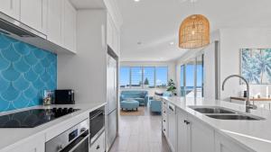 cocina con armarios blancos y pared de acento azul en Boronia Beach House One, en Sawtell