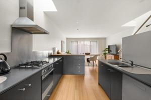 La cuisine est équipée de placards gris et d'un four avec plaques de cuisson. dans l'établissement South Yarra Luxe - Spacious Townhouse & Parking, à Melbourne
