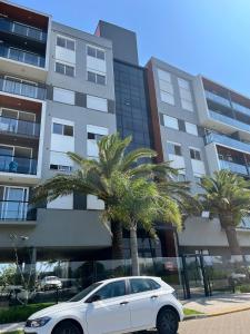 a white car parked in front of a building with palm trees at Apartamento alto padrão in Xangri-lá