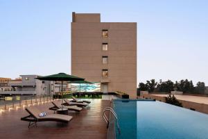 a hotel with a pool and chairs and a building at Ramada Encore By Wyndham Bhiwadi Phool Bagh Chowk in Bhiwadi