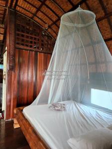 a bed with a mosquito net hanging over it at p2 เรือนกระท่อมน้ำ เรือนรอยน้ำ บ้านกามเทพ อัมพวา โฮมสเตย์ in Amphawa