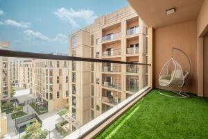 1BR Apartment With Balcony - 9 Mins to Sharjah Airport - Balcony Breeze في الشارقة: شرفة شقة مع أرجوحة وعشب