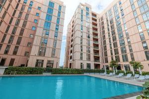 1BR Apartment With Balcony - 9 Mins to Sharjah Airport - Balcony Breeze في الشارقة: مسبح وسط مبنيين طويلين