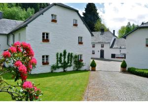 una gran casa blanca con un patio con flores rosas en Le Vieux Moulin Weywertz, en Bütgenbach