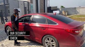 a man standing next to a red car at Eden Luxurious Apartments in Mosere Ikoga