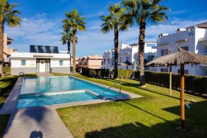 a swimming pool with palm trees and a building at Punta Prima 2 bed apartment with private garden in Punta Prima