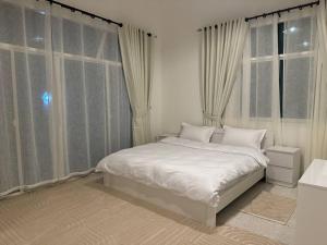 1 dormitorio con 1 cama blanca frente a las ventanas en Oasis Villa Stay by Lunar, en Abu Dabi