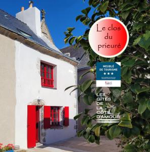 un cartello di fronte a un edificio bianco con finestre rosse di Le clos du prieuré - Les Gîtes de la Côte d'Amour a Batz-sur-Mer