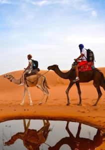 two people riding on camels in the desert at Nour Desert Luxury Camp in Merzouga