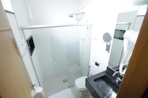 a white bathroom with a shower and a toilet at Hotel Pouso Novo in Matão