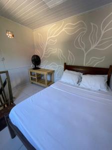 a bedroom with a white bed with a tree mural on the wall at Chalé caiçara aconchegante in Paraty