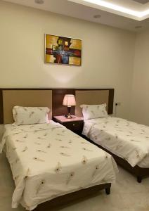 a bedroom with two beds and a table with a lamp at امواج الشرق للشقق المخدومه in Khamis Mushayt