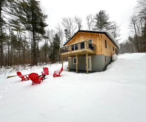 a house with two red chairs in the snow at The Mont Haus - Minutes to Mt Snow & Stratton! in Wardsboro