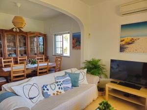 a living room with a white couch and a television at Casa das Oliveiras - piscina privada, jardim, perto da praia in Moncarapacho