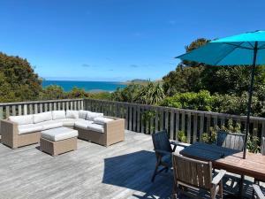 a deck with a couch and a table and an umbrella at Kaka Point Beach House in Kaka Point