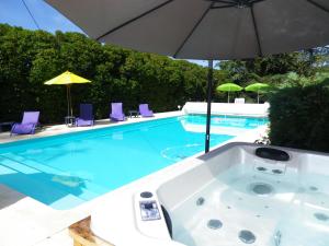 a bath tub with an umbrella next to a swimming pool at Séjour authentique-Piscine Privée Chauffée- Spa et Nature in Beauville