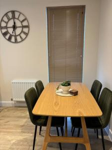 a dining room table with green chairs and a clock at 7 Thadan Apartments in Addlestone