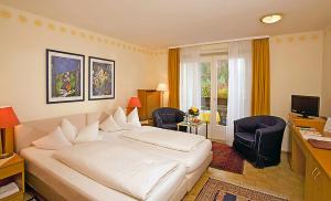 a bedroom with a white bed and a desk and chairs at NaturMed Hotel am Park in Badenweiler