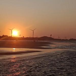 a sunset on a beach with windmills in the background at Casinha Azul in Estrela