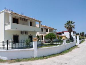 a white house with a fence and a palm tree at Ammos in Roda