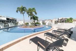a swimming pool with chairs and palm trees on a building at Modern Condo 200m from Beach & 5th Ave in Playa del Carmen