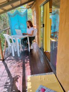 a woman sitting at a table with a laptop on a porch at Chalé Aconchego in Santo Antônio do Leite +111 photos