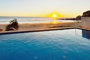 a swimming pool next to a beach with the sunset at Condo Playa & Waterfront Heated Alberca in Mazatlán