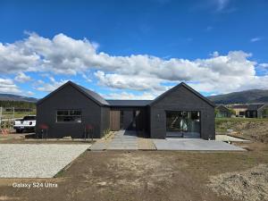 a black house in a field with mountains in the background at River Terrace Retreat Cromwell in Cromwell