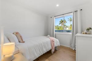 a white bedroom with a bed and a window at Bamboo Hideaway - 4 Mins Walk to the Beach in Culburra Beach