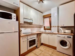 Una cocina con gabinetes blancos y lavadora y secadora. en Apartamento Las Gaviotas, en Comillas