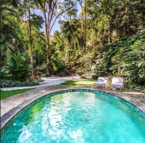 a swimming pool with two chairs in a forest at Exclusive Oásis by Lotta De Macedo Soares in Petrópolis