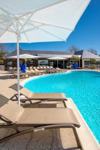 a swimming pool with lounge chairs and an umbrella at M&V Resort Camping in Langrune-sur-Mer