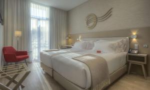 Un dormitorio con una gran cama blanca y una silla roja. en NH Collection Porto Batalha, en Oporto