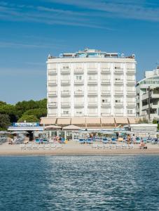 a large white hotel on the beach with chairs and the water at Hotel Acapulco in Milano Marittima