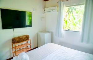 una camera da letto con un letto, una tv e una finestra di Pousada Coco Dendê a Ilha de Boipeba